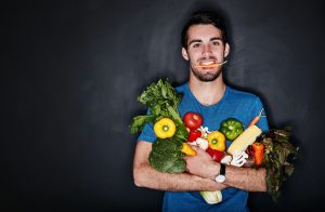 Studio portrait of a young man carrying an armful of healthy vegetables against a dark background